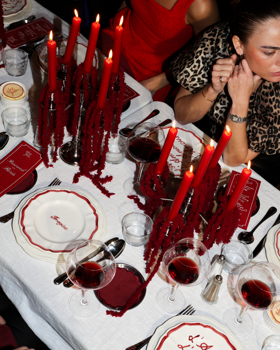 Chez Jules table styling by Imaginary Friends – red taper candles, scalloped plates, wine glasses and personalized dinner details in a bold red theme.