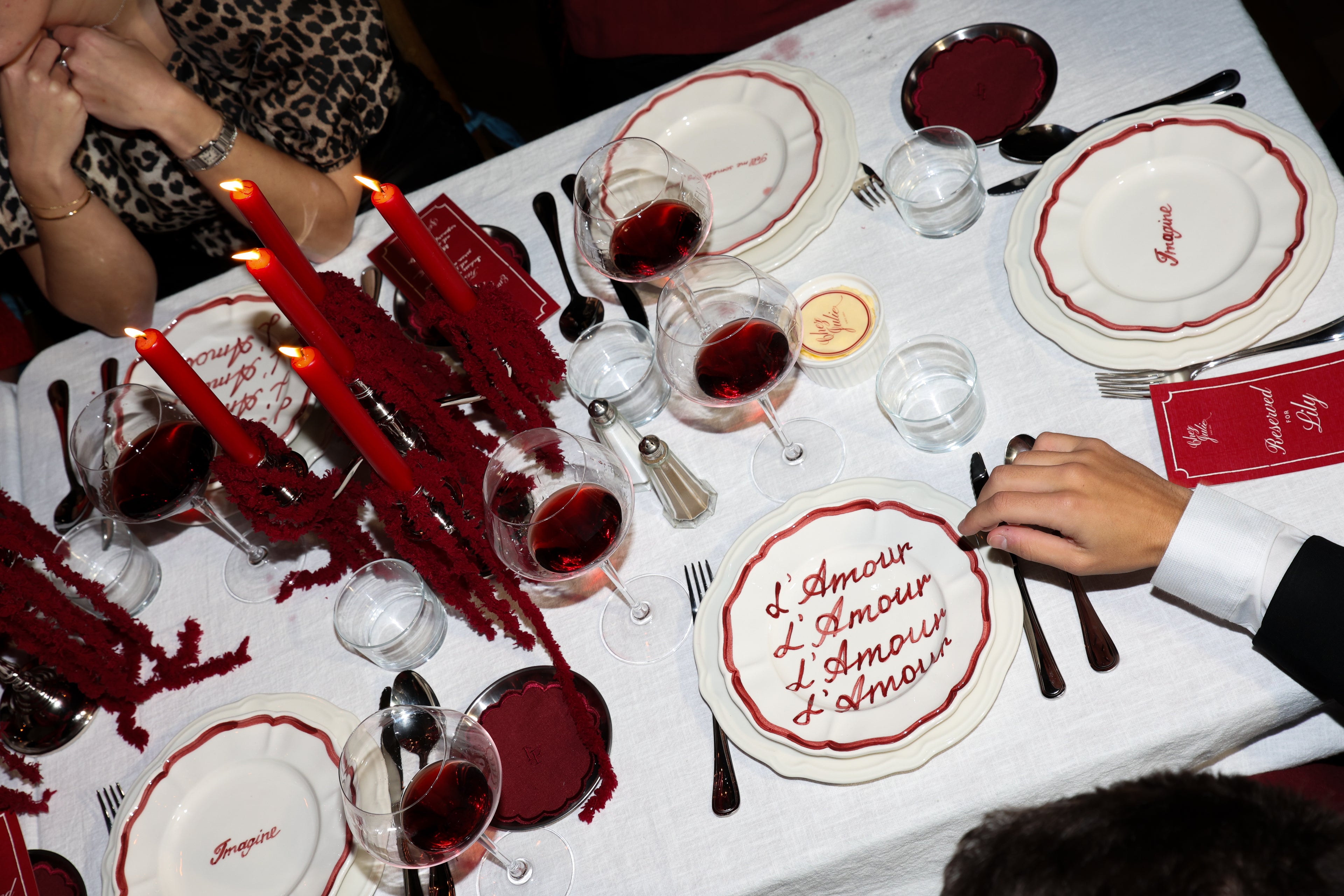 Chez Jules table styling by Imaginary Friends featuring red taper candles, personalized ‘L’Amour’ plates, red wine glasses, and layered white tableware on a crisp white tablecloth.