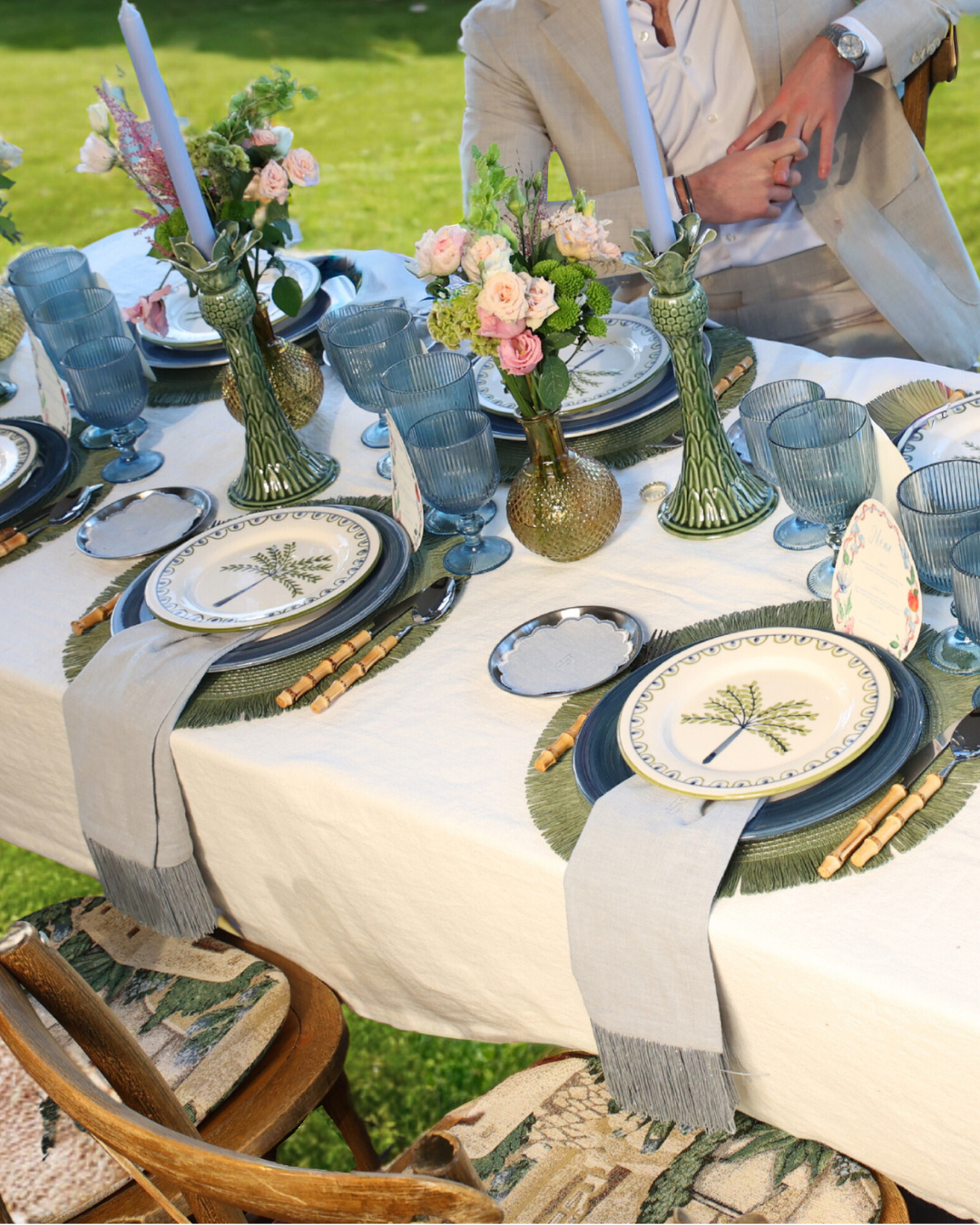 Imaginary Friends Isla Bonita table styling – palm-tree plates, blue ribbed glassware, floral centre pieces and raffia details in an outdoor summer setting.