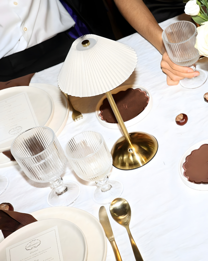 The Suite table styling by Imaginary Friends with a gold table lamp, ribbed clear glassware, white plates, brown scalloped side plates and brown linen napkins.
